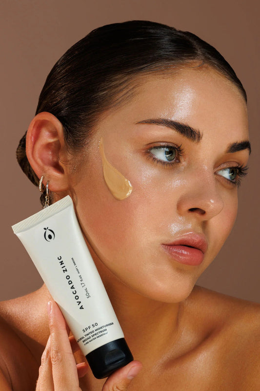 Woman applying Avocado Zinc sunscreen to her face with a brown background